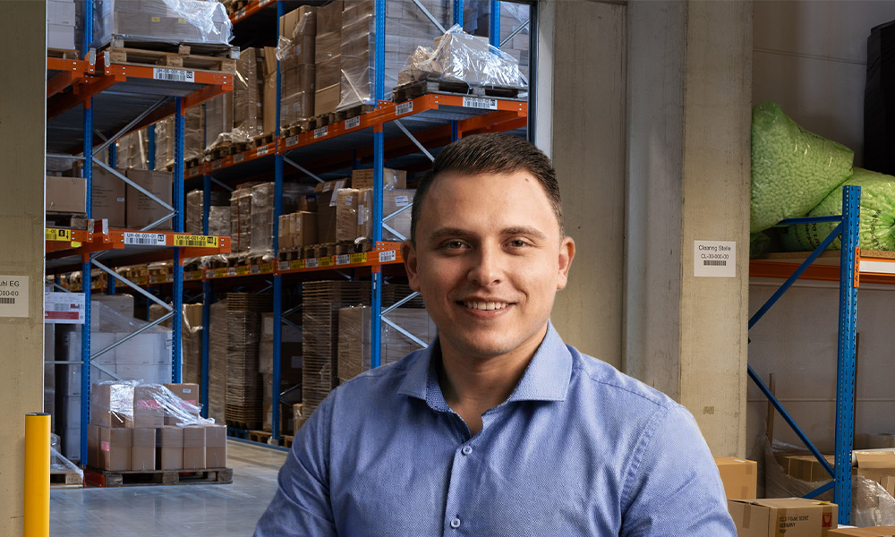 Stefan Schmidt von Greim Consulting, einem auf Prozessoptimierung, Supply Chain und Fulfillment spezialisierten Beratungsunternehmen, im Lager mit Regalen voller Verpackungen, die die logistischen Abläufe des Unternehmens abbilden.